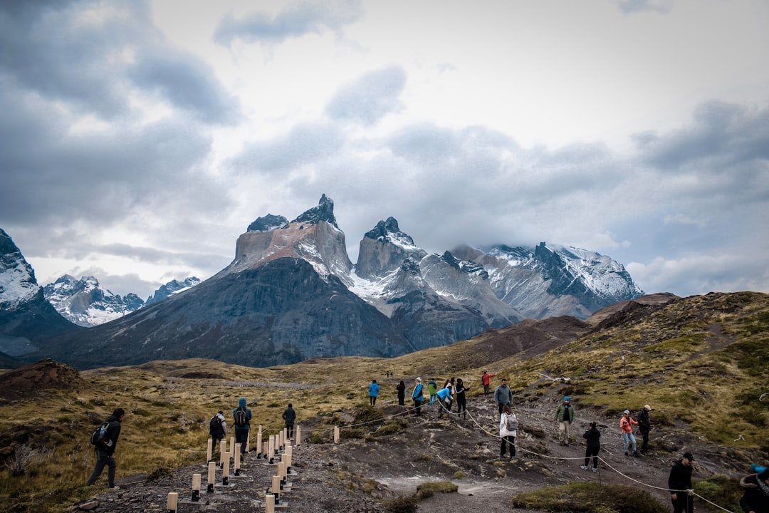 Hikers ascending steep rocky trail toward Torres del Paine towers with dramatic clouds